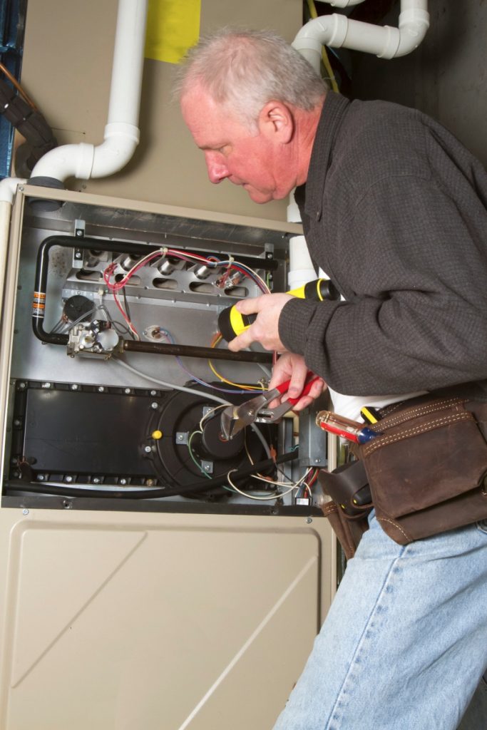 mature man with gray hair wearing long sleeved shirt and denim jeans holds monkey wrench and flashlight to adjust heating furnace parts